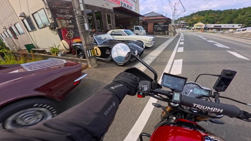 Motorcycle rider passing a collection of classic American cars outside a garage in Ozu, Ehime