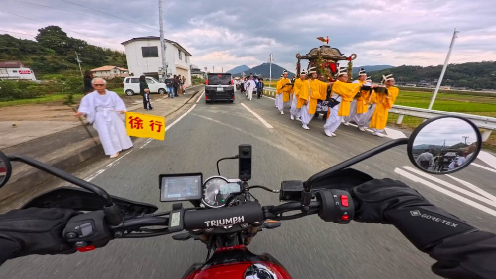 Motorcycle passing a traditional Japanese festival procession carrying a mikoshi in rural Ehime
