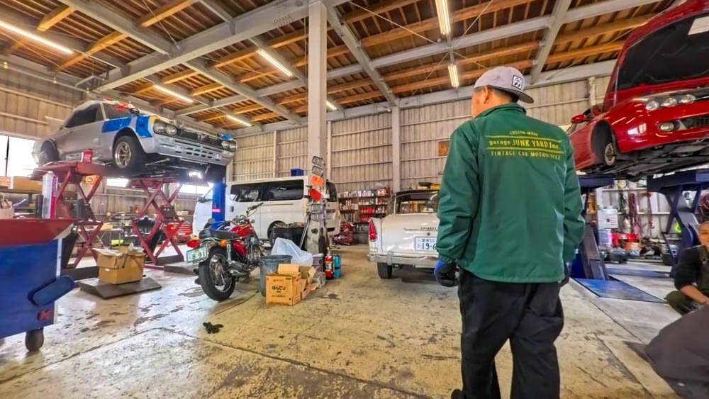 Inoue-san inside a workshop filled with classic cars and motorcycles in Ozu, Ehime