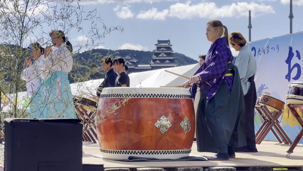 Performers on an outdoor festival stage with Ozu Castle visible in the background