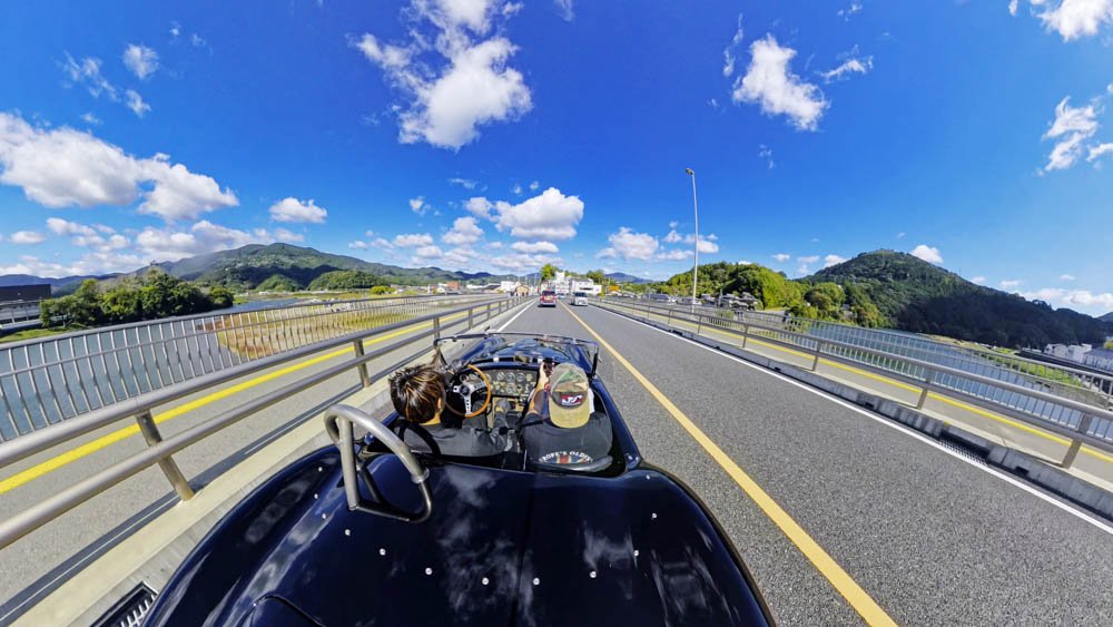 View from the rear of a black Shelby Cobra driving through Ehime during Adam’s first ride in the car