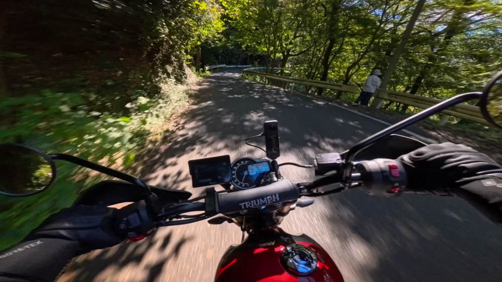 First-person view from a Triumph motorcycle riding a narrow forest road in Ehime