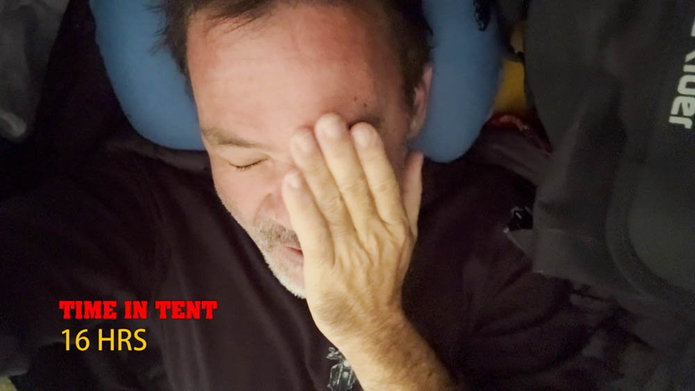 Exhausted motorcycle traveler inside a tent after hours of severe wind and rain in Ehime