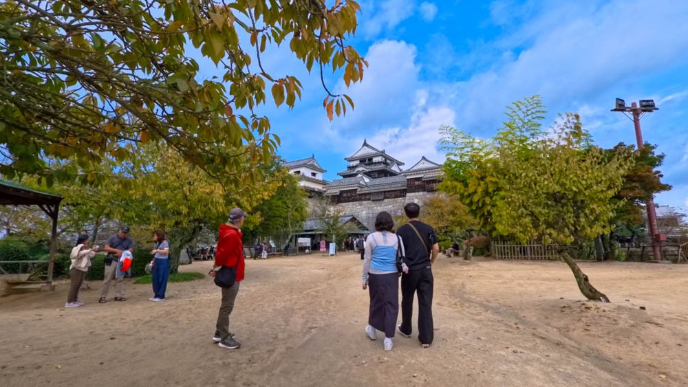 Visitors approaching historic Matsuyama Castle surrounded by trees in Ehime, Japan