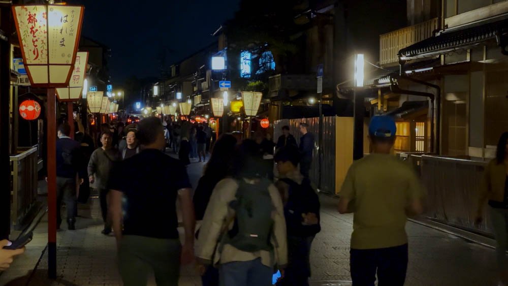 Crowds walking beneath traditional lanterns through Gion in Kyoto at night
