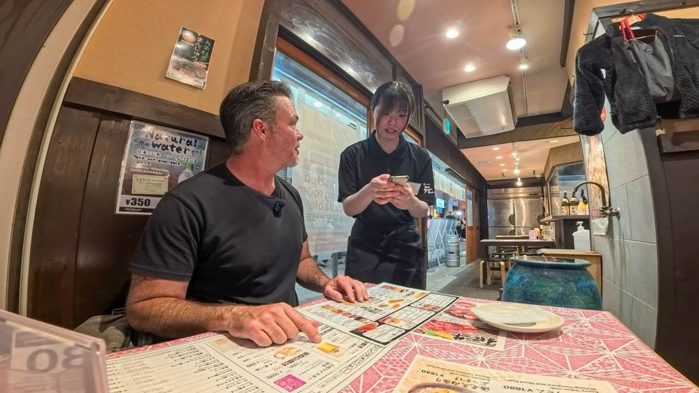 Adam ordering food from a young restaurant worker while exploring Kyoto on foot