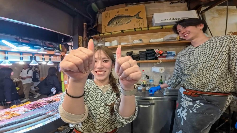 Smiling young seafood stall workers giving a thumbs-up at Nishiki Market in Kyoto
