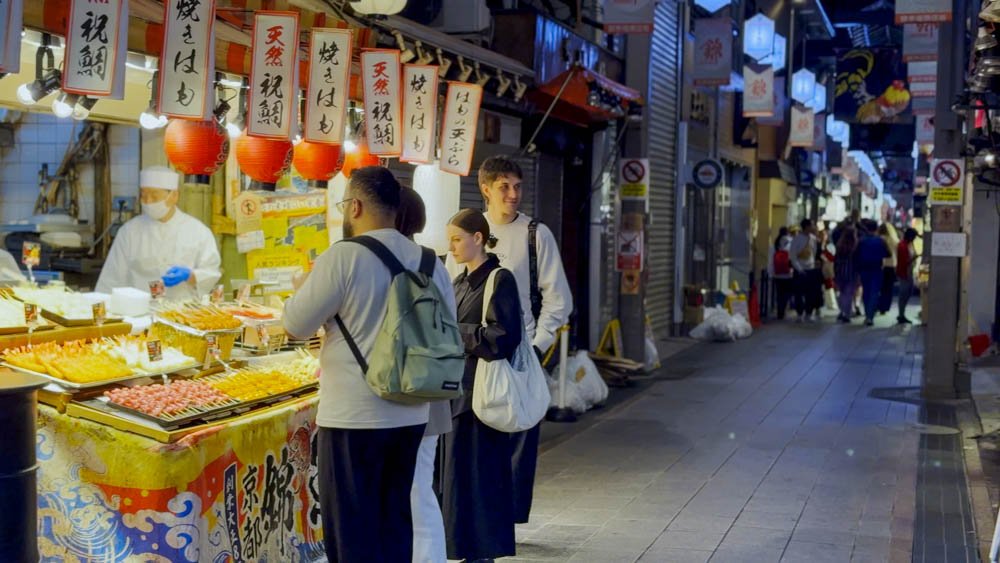 Visitors browsing illuminated food stalls inside Nishiki Market in Kyoto during the evening