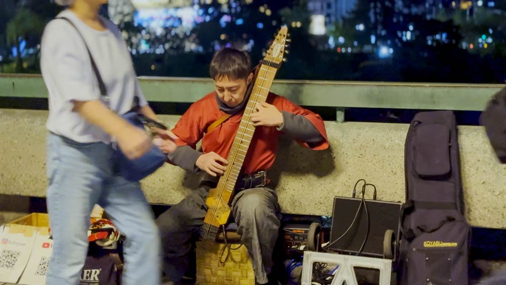 Street musician playing an unusual string instrument at night in Kyoto