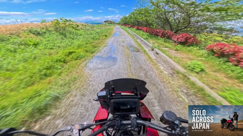 Motorcycle riding along a wet gravel road through farmland in Shiga